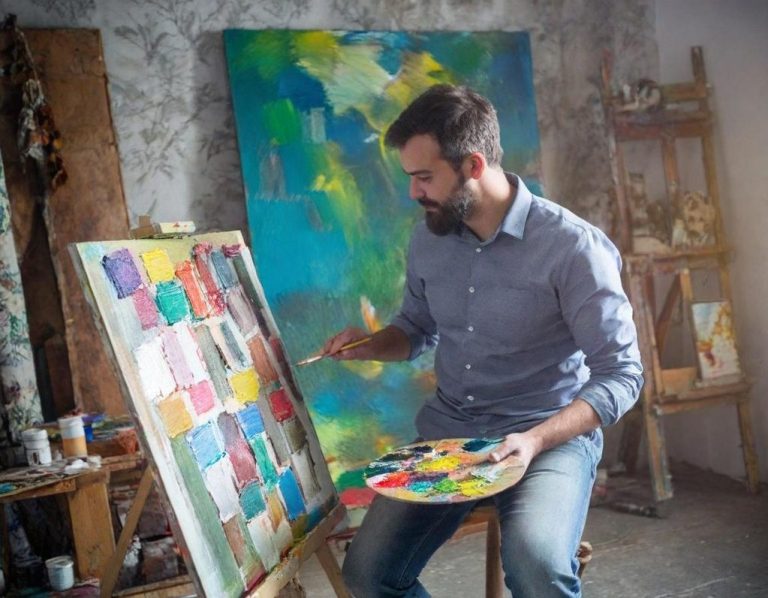 Ein Künstler malt an einer Staffelei mit bunter Farbpalette in einem Atelier.