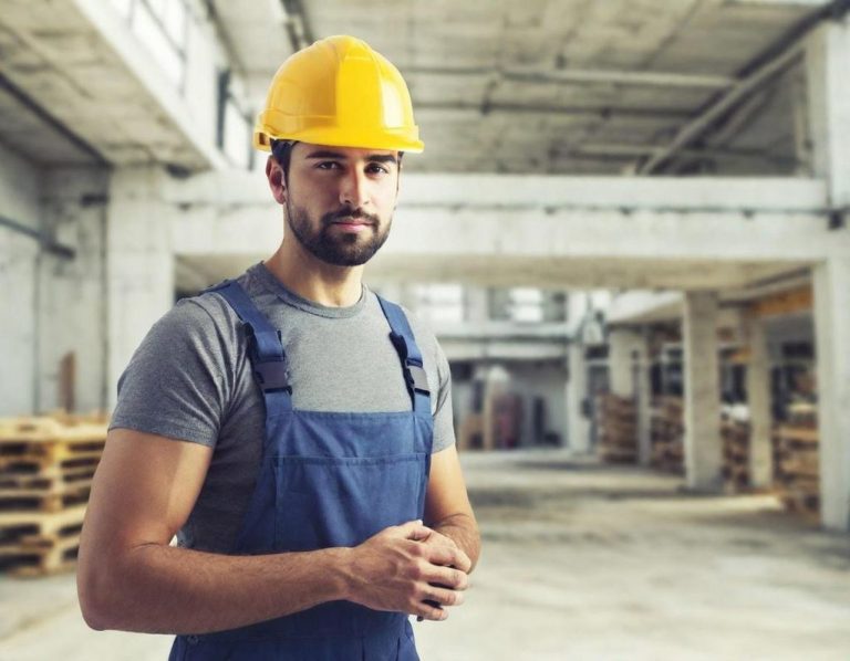 Mann in Arbeitskleidung und Schutzhelm in einer Lagerhalle.